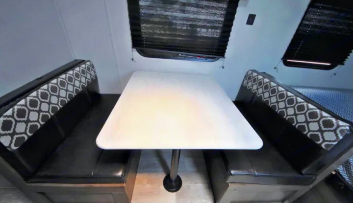 RV rental interior: A bright dinette with a white table and black patterned booth seats provides a cozy dining space.. Prime Time Avenger 2021
