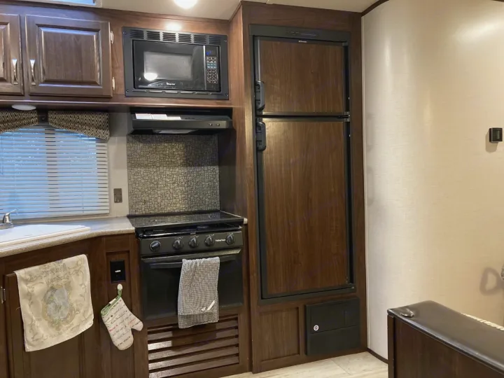 Kitchen area of an RV rental with microwave, stove, sink, and wood-paneled refrigerator. Ready for your next adventure!. Palomino Solaire Ultra Lite 2017