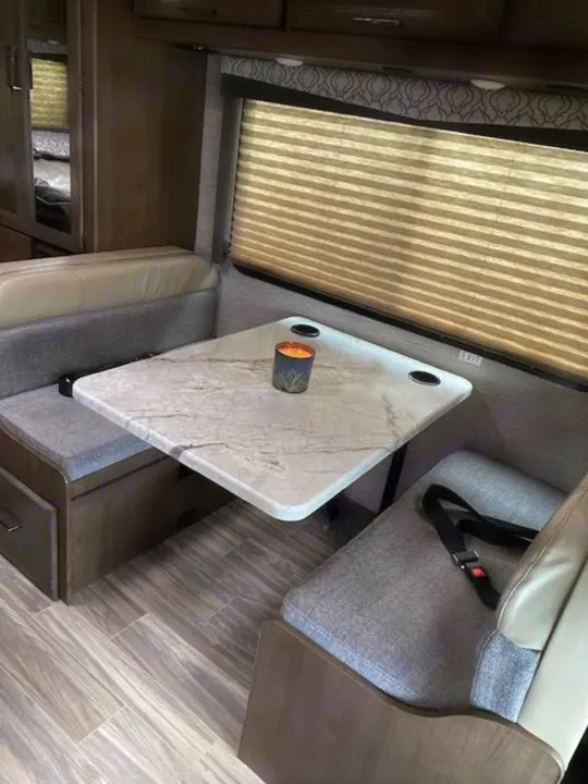 Cozy RV rental dinette with a marble-look table, comfortable seating, and window blinds. Perfect for dining on the go.. Thor Motor Coach Freedom Elite 2021