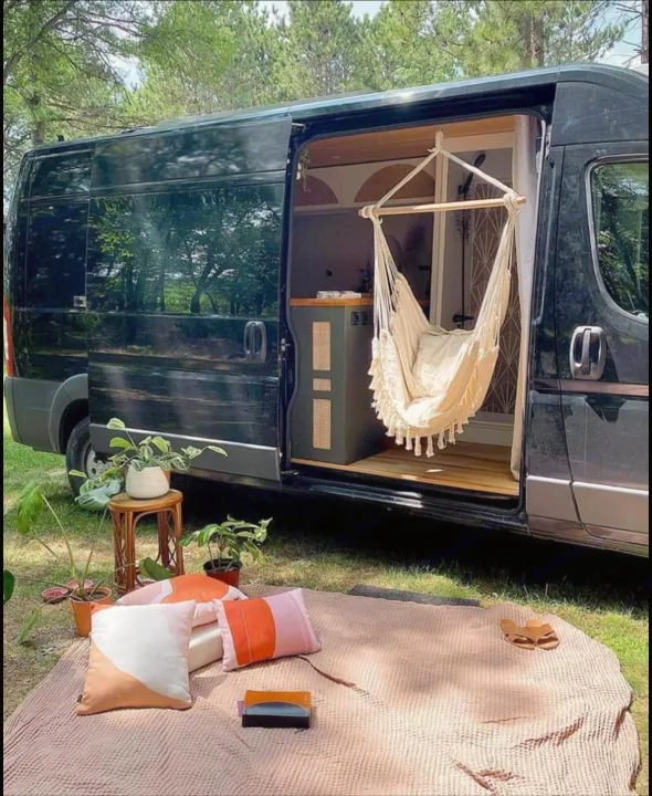 RV rental: Black camper van with open door, featuring a hanging chair & cozy outdoor picnic setup on grass. Perfect for nature escapes.. Other Other 2015