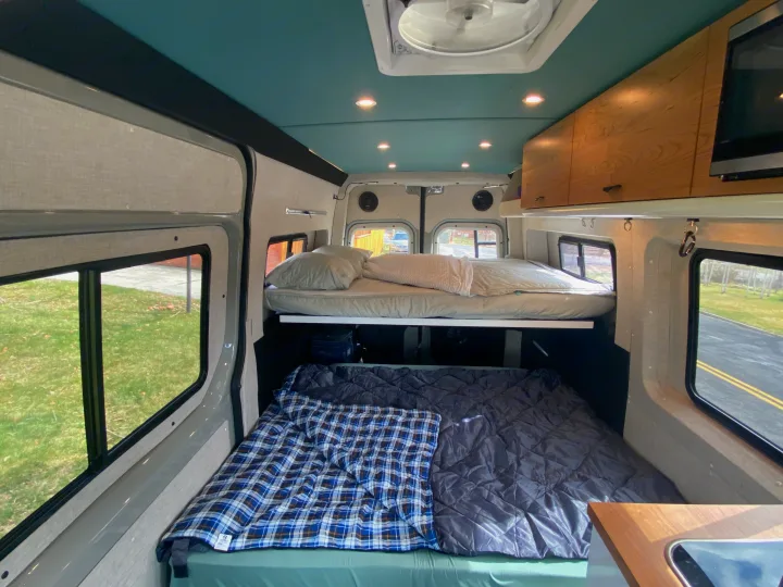 Bright RV rental interior with elevated and floor beds, wood cabinets, and a teal ceiling with lights.. Mercedes-Benz Sprinter 2020