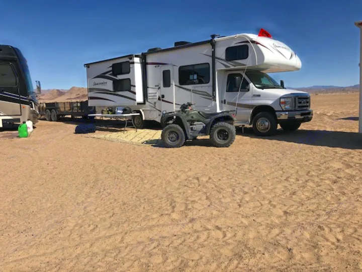 White RV rental and green ATV parked on sandy desert terrain. Ready for off-road adventures and remote camping.. Forest River Sunseeker 2017