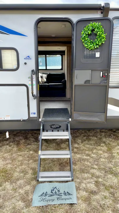 Welcoming travel trailer RV rental entrance: open door with wreath, multi-step stairs, and a 'Happy Camper' mat.. Forest River Cherokee 2021