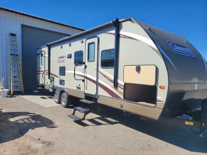 Explore with this Coleman RV rental! A large, modern travel trailer parked by a building on a bright day.. Dutchmen Coleman 2017