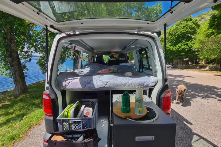 RV rental adventure! This camper van shows a cozy bed & kitchen setup by a lake with a dog nearby.. Volkswagen T6 2020