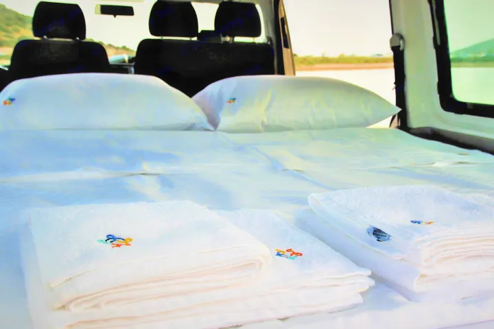 Inside a spacious RV rental, a comfy bed with crisp white linens and fresh towels awaits your next travel adventure.. Volkswagen T6 2020