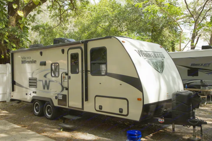 A light-colored Winnebago Micro Minnie travel trailer, ready for an RV rental, parked at a leafy campground.. Other Other 2019