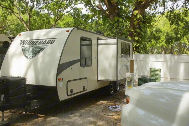 A spacious Winnebago travel trailer, ideal for an RV rental, parked under trees with its slide-out extended at a scenic campsite.. Other Other 2019