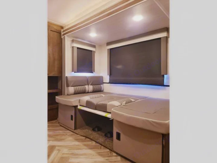 Modern RV rental interior: grey convertible dinette/bed, blackout shades, and wood-look floor for versatile living.. Forest River Wildwood 2021
