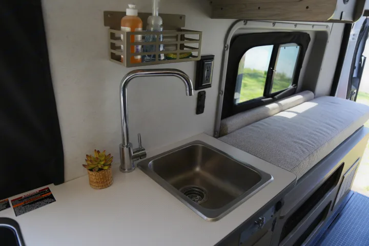 Compact RV rental kitchen with sink, faucet, and storage, ideal for road trips and small space living.. Winnebago Solis 2021