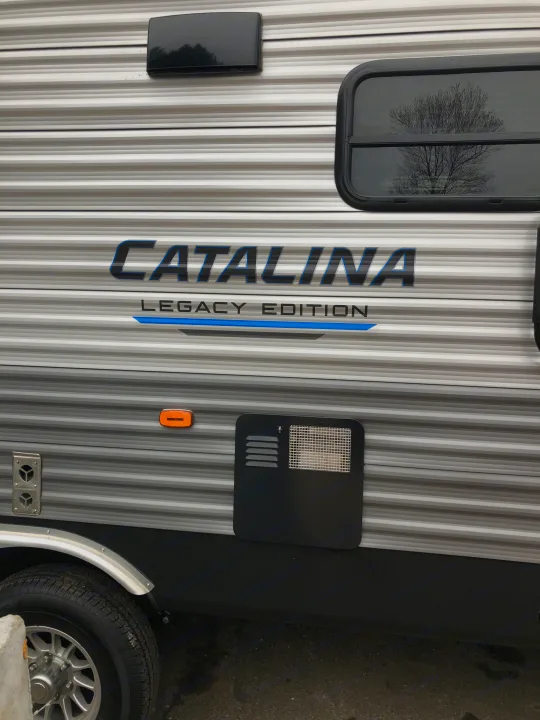 Side view of a "CATALINA LEGACY EDITION" rv rental, featuring striped siding, reflective window, and utility panels.. Coachmen Catalina 2021