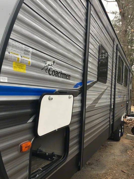 An RV rental, a grey Coachmen travel trailer, with its side storage door open revealing interior space.. Coachmen Catalina 2021