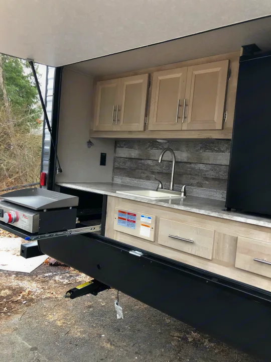 Explore this RV rental's outdoor kitchen! Features a pull-out griddle, sink, cabinets, and mini-fridge for convenient camping.. Coachmen Catalina 2021