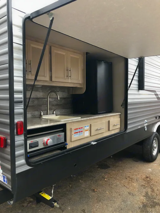 This RV rental's outdoor kitchen features a sink, fridge, cabinets, and a pull-out griddle for convenient camping.. Coachmen Catalina 2021