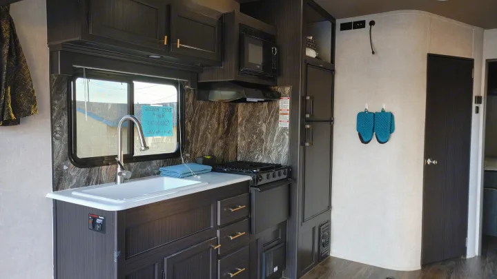 This clean RV rental kitchen features a modern sink, stove, microwave, and fridge, ideal for road trips.. Other Attitude 2021