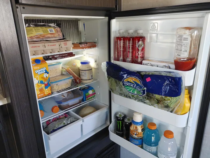 An open rv rental fridge, well-stocked with eggs, bacon, juice, sparkling drinks, melons, and condiments for a road trip.. Other Attitude 2021