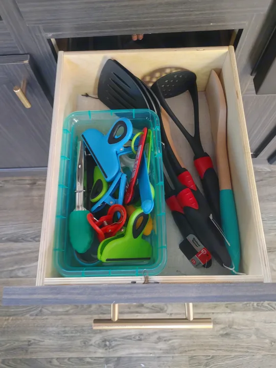 Open drawer in an RV rental, showing kitchen spatulas, wooden spoons, and colorful food clips for organized storage.. Other Attitude 2021