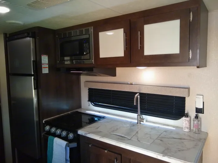 RV rental: fully equipped kitchen with refrigerator, microwave, stove, sink, and stylish dark wood cabinets.. KZ Sportsmen 2021
