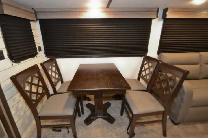 Spacious RV rental dining area: dark wood table, four comfy chairs, light walls, and blinds create a cozy interior.. Crossroads Other 2021