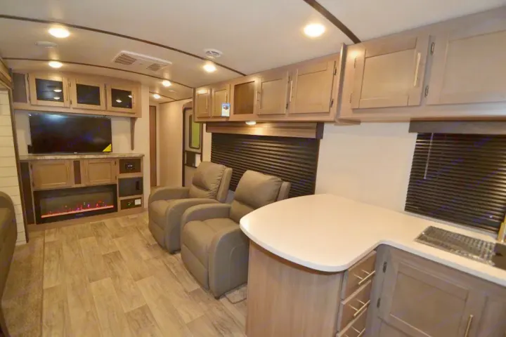 Inside a modern RV rental: comfortable recliners, large TV, fireplace, overhead cabinets, and a compact kitchen counter.. Crossroads Other 2021
