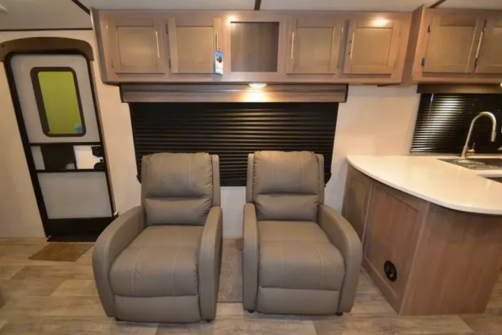 RV rental interior highlighting two comfortable gray recliners, overhead cabinets, and a compact kitchen with a sink.. Crossroads Other 2021
