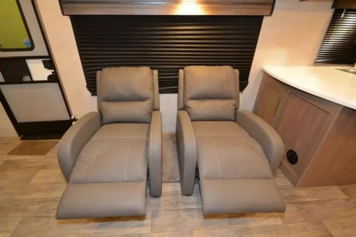 Inside an RV rental: two comfy extended recliners, wood floors, kitchen counter, and blinds for relaxation.. Crossroads Other 2021