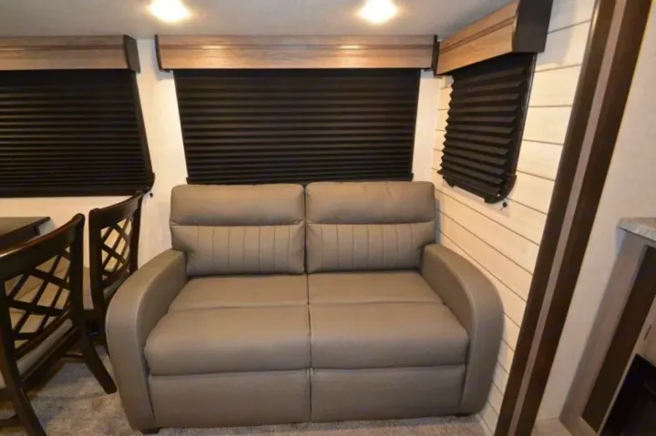 Inside a modern **RV rental**: gray sofa, dining table & chairs, plus dark pleated window blinds providing privacy.. Crossroads Other 2021
