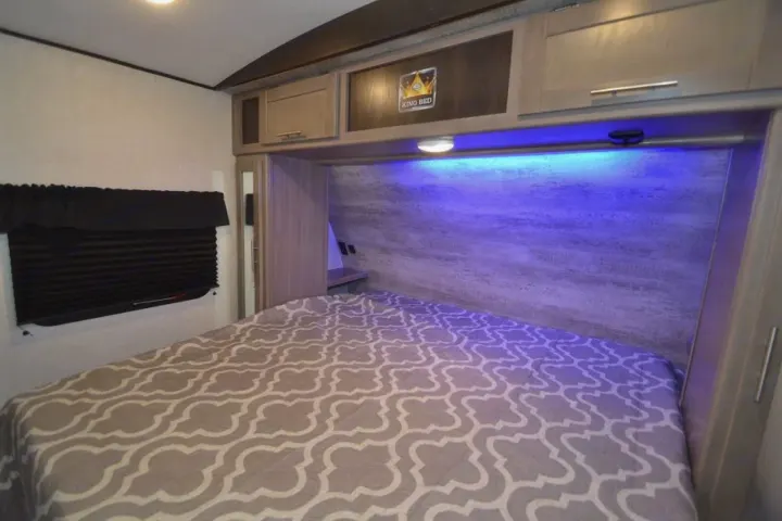 Cozy RV rental bedroom with a king bed, overhead storage, ambient blue lighting, and a large window.. Crossroads Other 2021