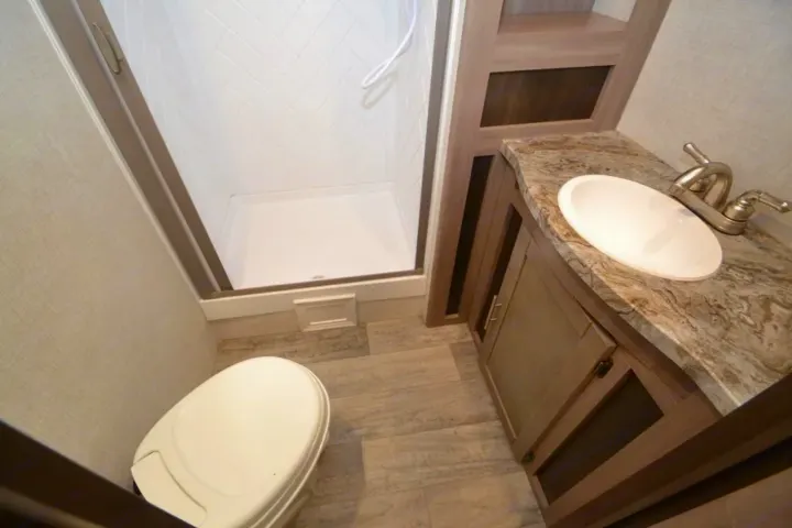 Modern RV rental bathroom: toilet, shower with herringbone tiles, vanity, sink, and wood-look flooring.. Crossroads Other 2021