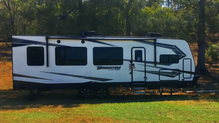 White Momentum G-Class RV rental, a travel trailer with black graphics, ready for camping outdoors.. Grand Design Momentum 2020