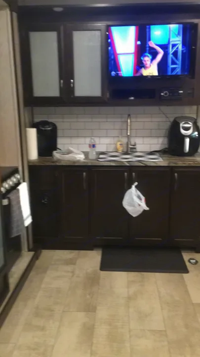 RV rental interior: kitchen with air fryer, TV airing game show, dark cabinets & light walls. Cozy living space.. Grand Design Momentum 2020