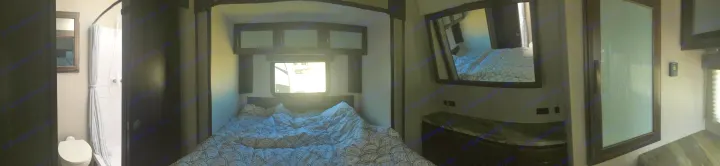Compact RV rental interior featuring a cozy bedroom with a patterned bed, a private toilet and shower, and mirrored storage.. Grand Design Momentum 2020