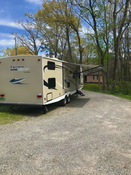 Beige Coachmen Freedom Express RV rental with extended awning, parked on gravel surrounded by trees.. Coachmen Freedom Express 2018