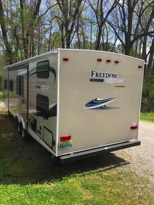 Tan Coachmen Freedom Express RV rental parked at a campsite, with trees and grass.. Coachmen Freedom Express 2018