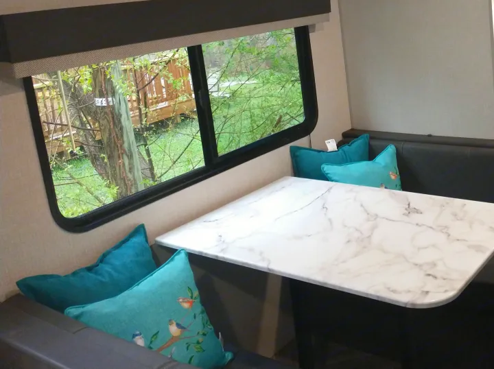 **RV rental** interior: A cozy dinette with marble-look table & teal cushions, offering a peaceful window view.. KZ Sportsmen 2021