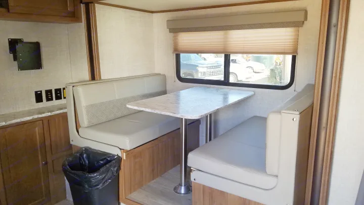 RV rental dinette: Light-colored benches with patterned backrests and a faux marble table. Includes a window, TV mount, and compact living space.. Gulf Stream Gulf Breeze Ultra Lite 2021