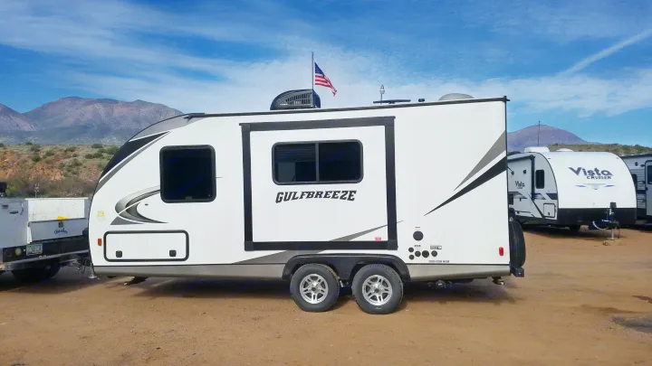 White Gulfbreeze travel trailer RV rental with American flag, parked in a desert setting with mountains and other RVs.. Gulf Stream Gulf Breeze Ultra Lite 2021
