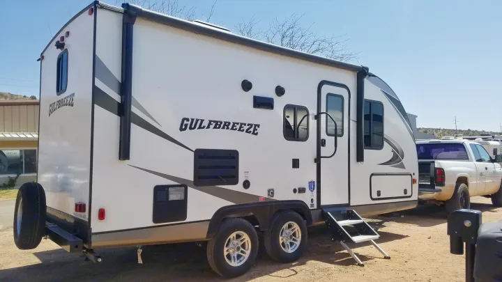 White Gulfbreeze travel trailer RV rental. Side view of this two-axle camper with extended steps & a rear tire.. Gulf Stream Gulf Breeze Ultra Lite 2021