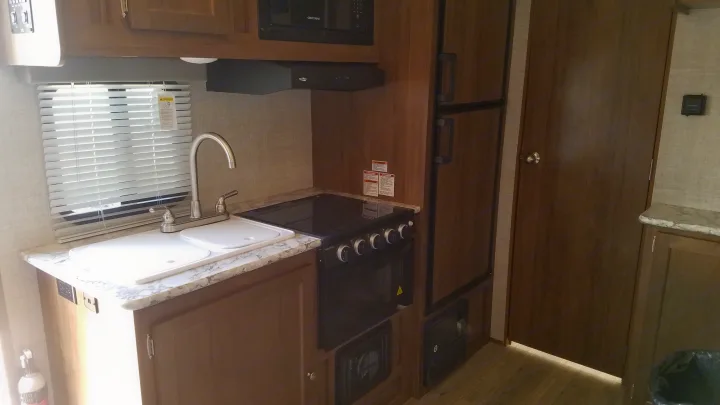 RV rental interior: a compact kitchen with a sink, microwave, stove/oven, and refrigerator. Plenty of wood cabinetry.. Gulf Stream Gulf Breeze Ultra Lite 2021