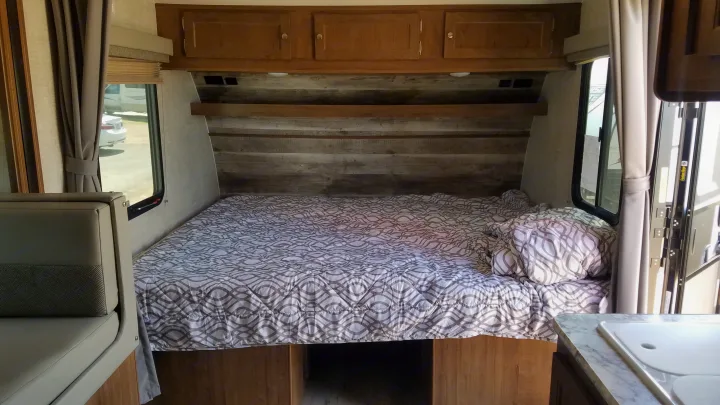 Interior of an RV rental showing a cozy bedroom with patterned bedding, overhead wood cabinets, and side windows.. Gulf Stream Gulf Breeze Ultra Lite 2021