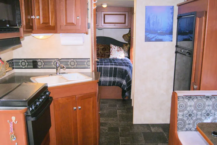 This RV rental interior features a compact kitchen with stove and sink, a cozy bed, and dinette seating for travel.. Winnebago Vista 2013