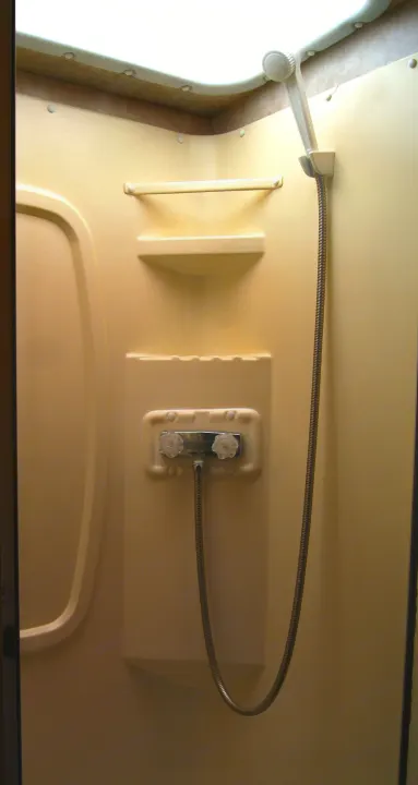 Clean RV rental shower with a handheld sprayer, temperature knobs, and storage shelves in an off-white stall.. Winnebago Vista 2013