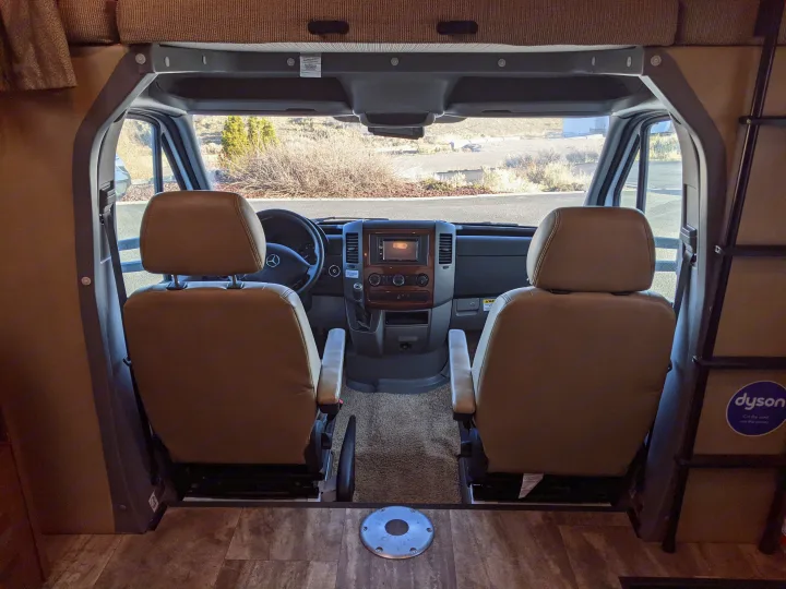 RV rental cockpit view with light brown driver and passenger seats, dashboard, and a clear view out the windshield.. Forest River Sunseeker 2016