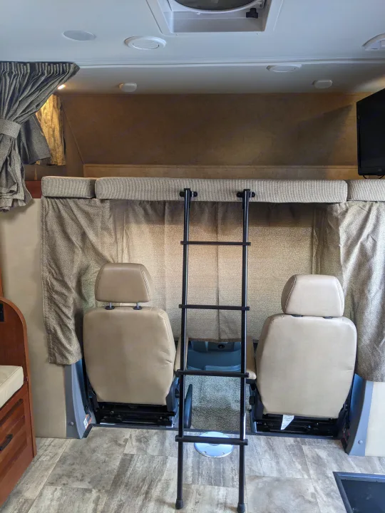 Spacious RV rental interior featuring front seats, an overhead bunk with ladder, curtains, and vinyl flooring.. Forest River Sunseeker 2016