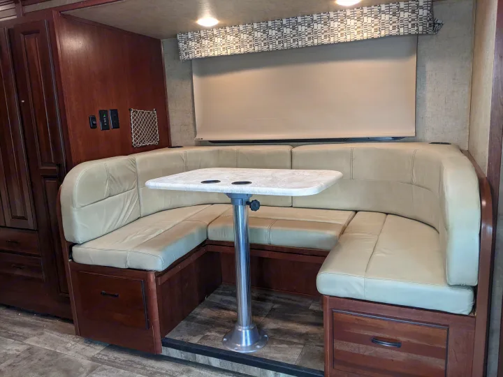 Spacious RV rental dinette with light leatherette booth seating, a table with cupholders, dark wood cabinetry, and window shade.. Forest River Sunseeker 2016