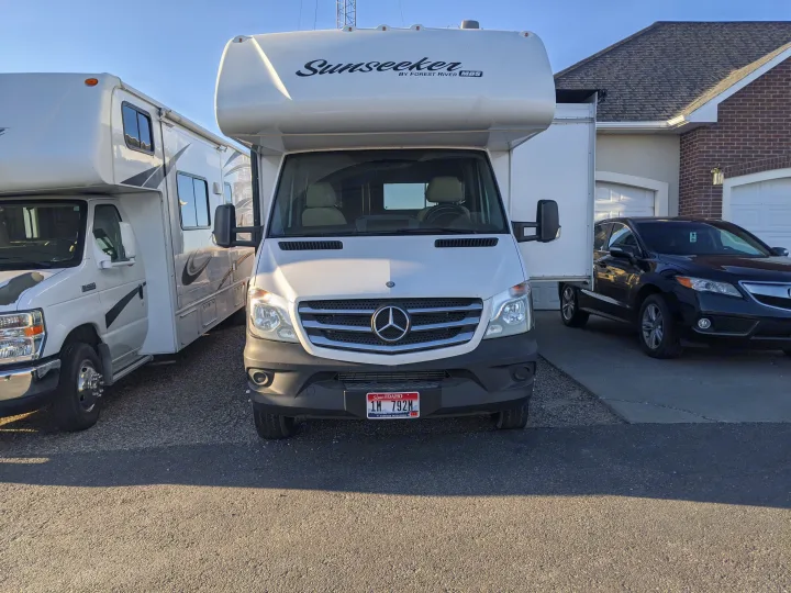 White Mercedes-Benz Sunseeker RV for RV rental, parked in a driveway near another RV and car by a home.. Forest River Sunseeker 2016