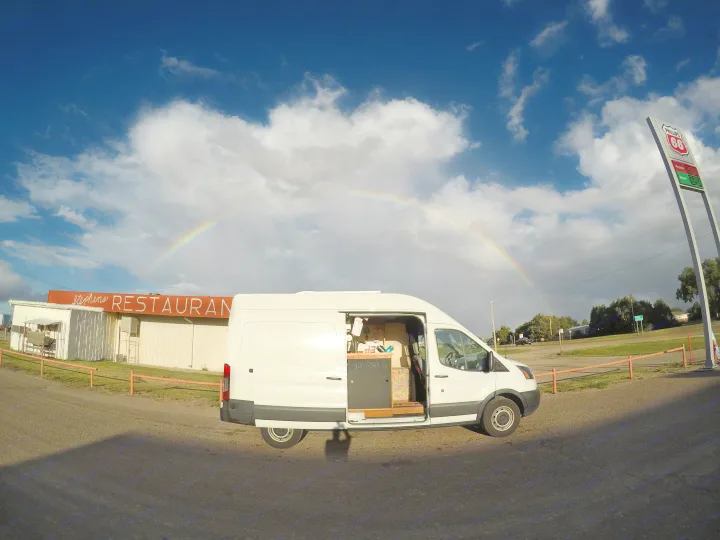 White camper van (RV rental) under a vibrant rainbow near Stephens Restaurant and Phillips 66 sign.. Ford Transit 2017