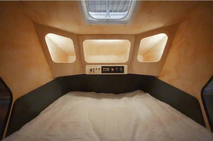 Cozy RV rental interior: bed, overhead cubbies, and a control panel. Compact, light wood paneled camper bedroom with skylight.. Polydrop K-20 2020