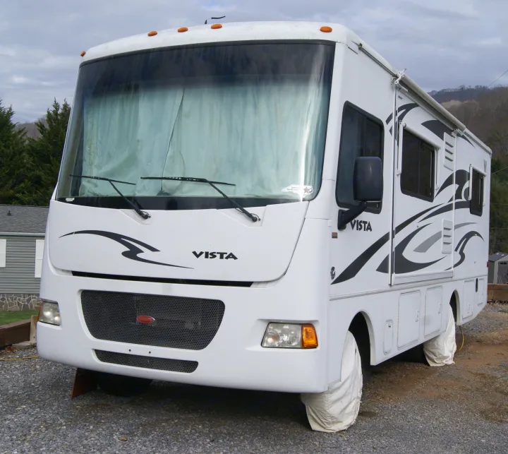 This white Class A "VISTA" recreational vehicle (RV), ideal for rv rental, is parked on gravel with tire covers & shaded windshield.. Winnebago Vista 2013