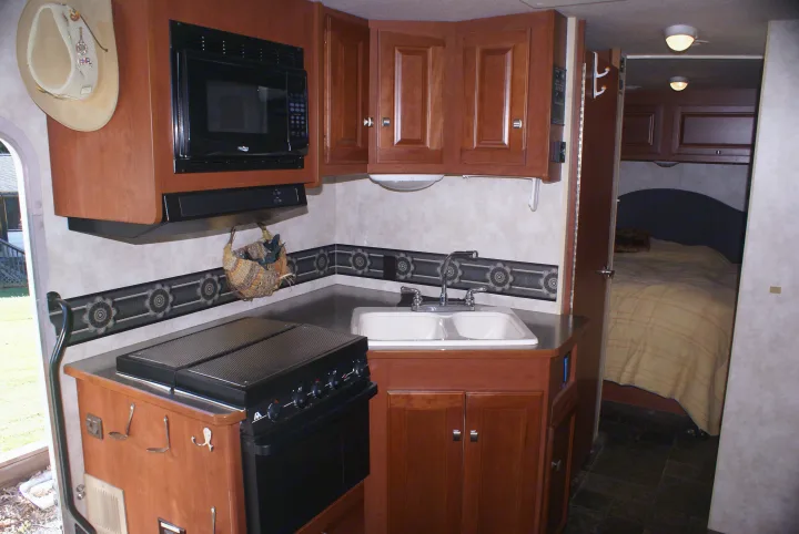 Inside a cozy RV rental: kitchen with microwave, stove, and sink, along with a bedroom beyond.. Winnebago Vista 2013